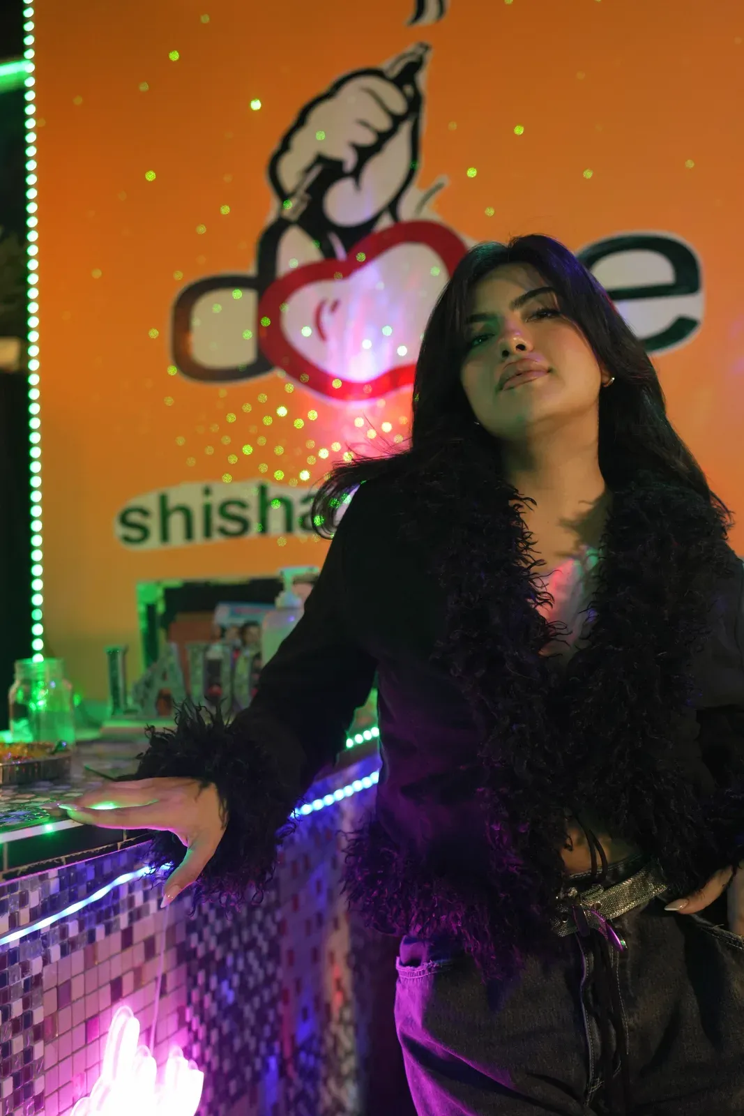 A guest standing at the mosaic bar at Dose Shisha, under the lit DOSE shisha lounge sign and the green LED strip